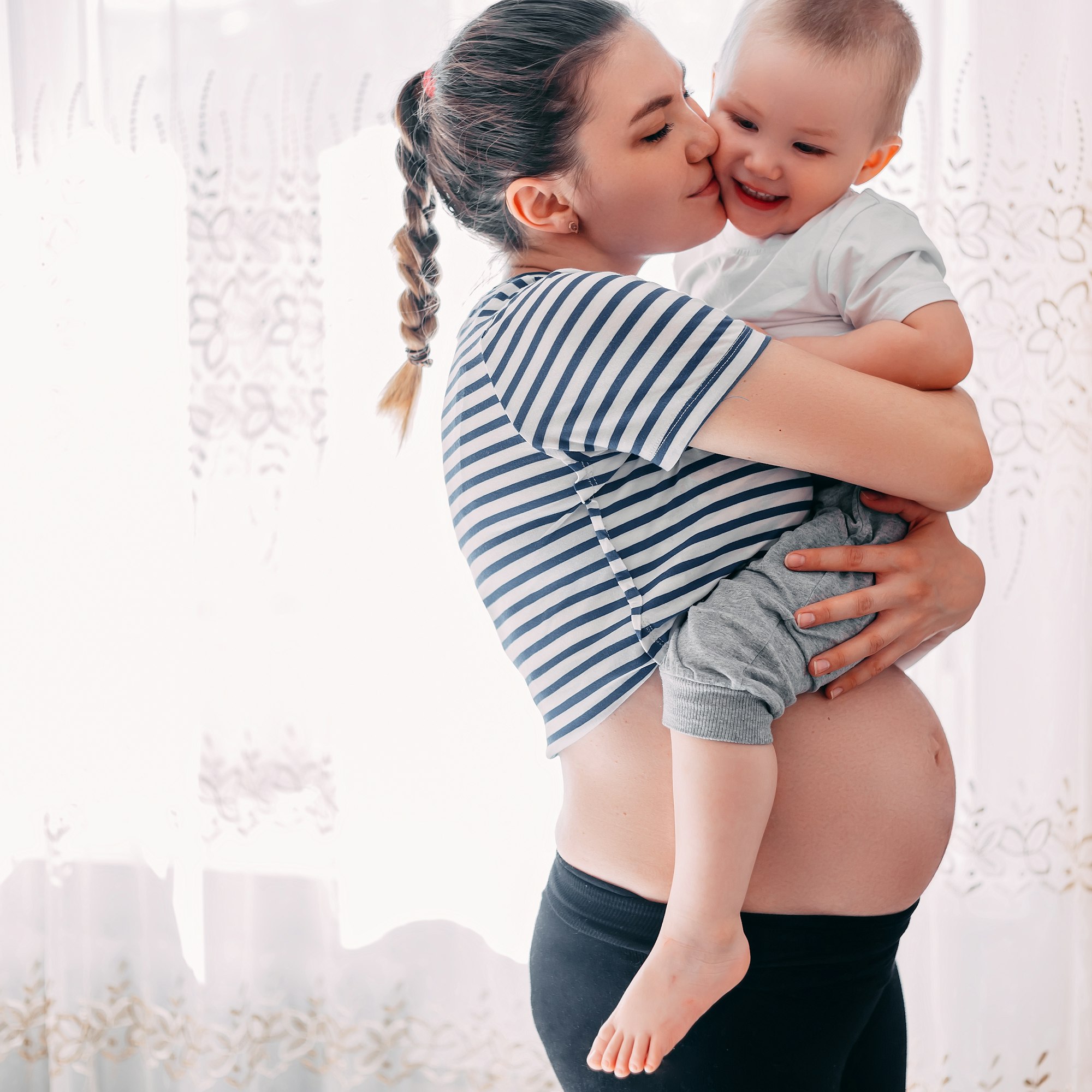 Pregnant women holds her first child. Eldest kid in arms. Elder brother