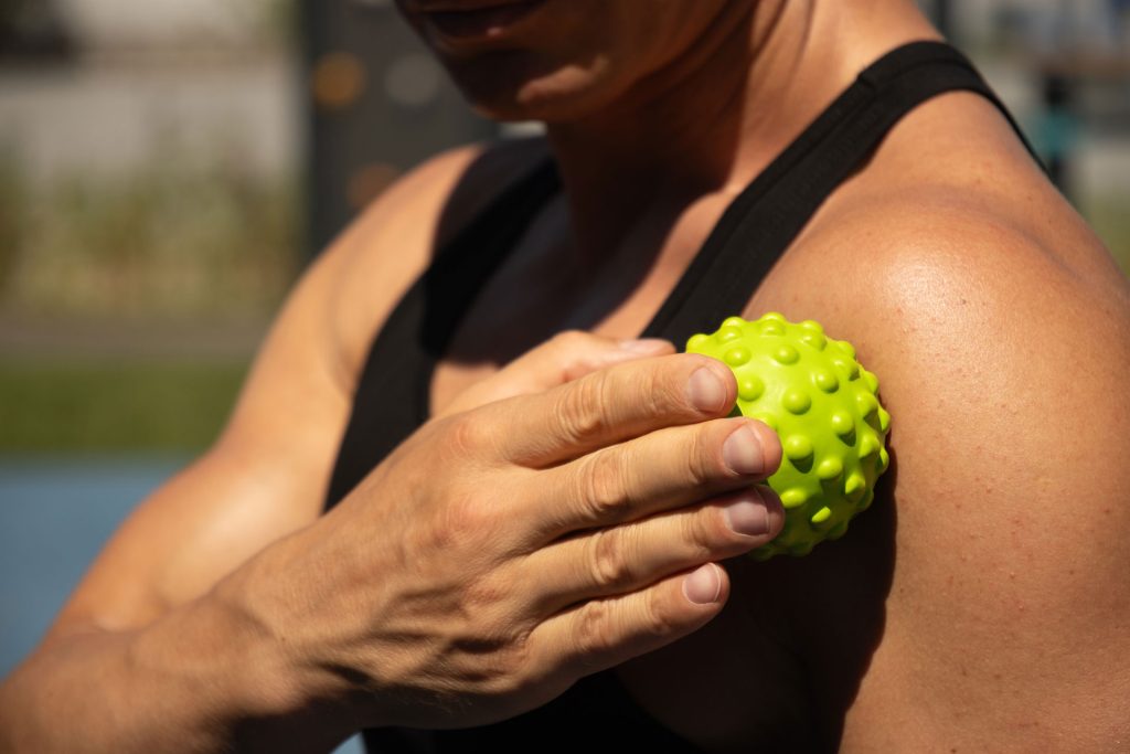 Man outdoor massaging his shoulder with a ball.